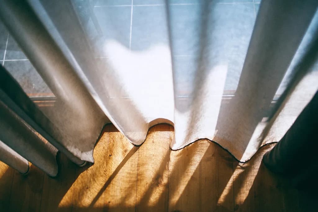Lumière du matin traversant un rideau de lin sur un parquet